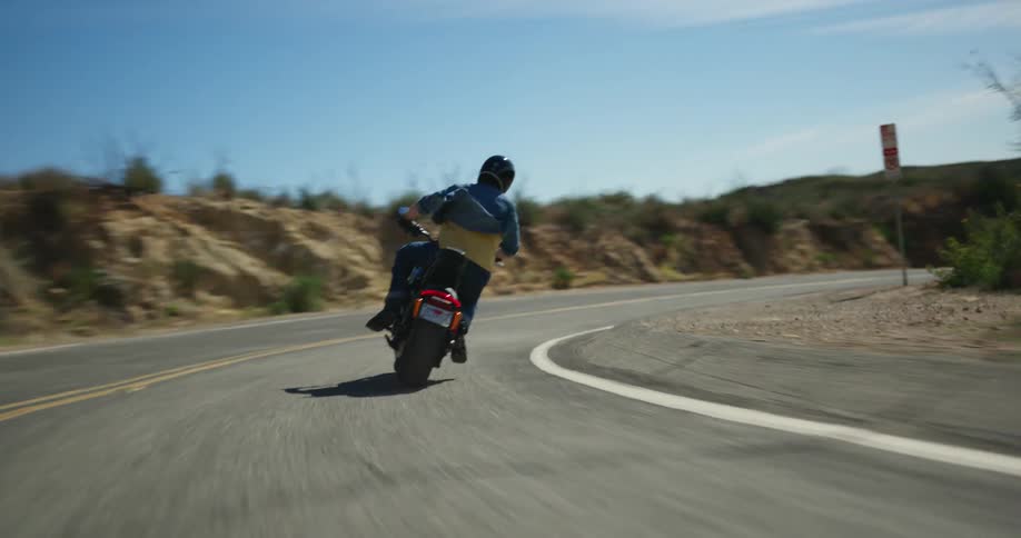 Male biker wearing black helmet blue shirt and jeans rides motorcycle on mountain highway