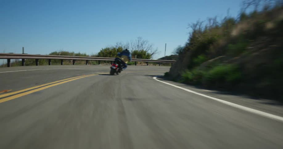 Man with helmet blue shirt and jeans rides motorcycle up mountain highway
