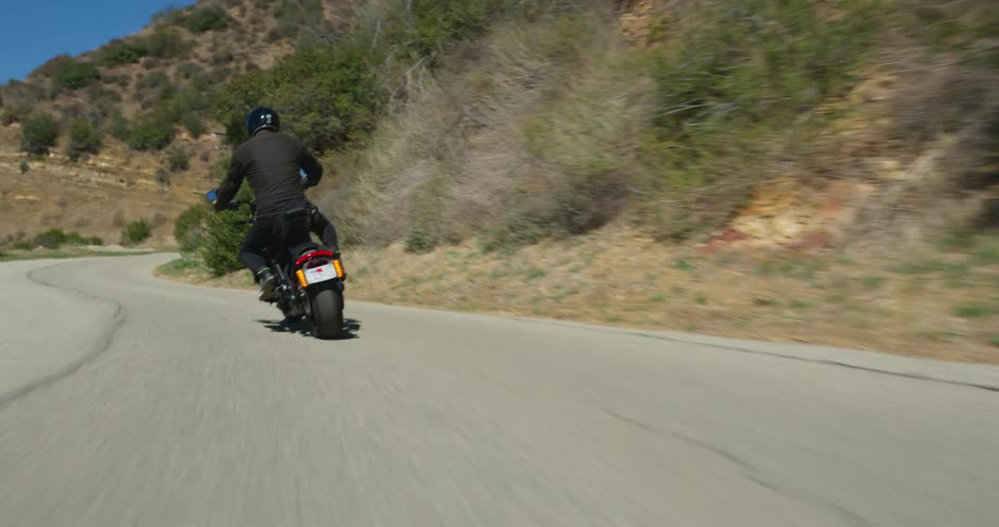 A man wearing dark apparel drives his motorcycle along a bending road