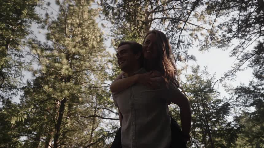 A man gives a woman a piggy back ride in the forest