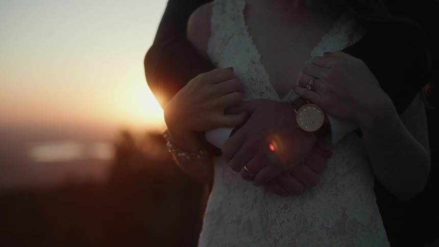 Sunlight shines behind a formally dressed couple huging each other near the top of a mountain at evening