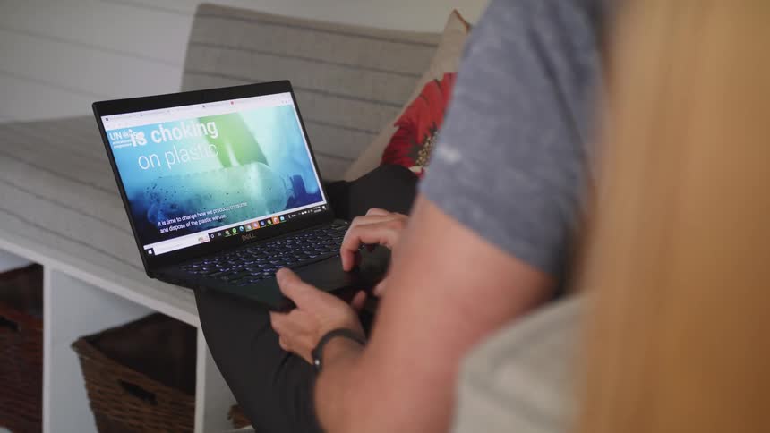 A man is scrolling on a laptop computer that is sitting in his lap