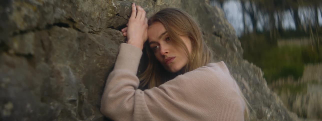 A sad looking woman leans against a large rock