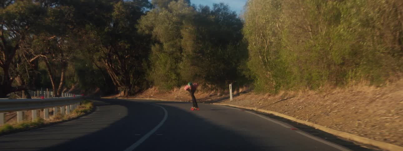 A skater bent forward in racing form skates on an empty curving rural road