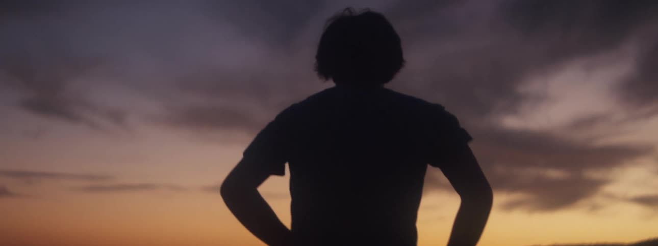 Boy running in field is silhouetted against the red sky at dusk