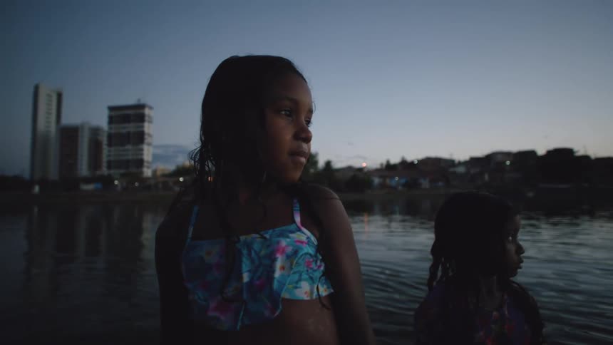 Two little girls stand in a large lake looking out into the distance and then looking at the camera