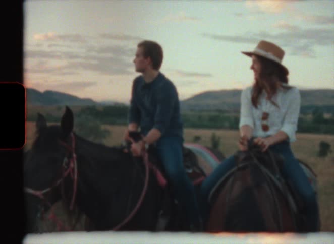 Young couple leisurely riding horses on the plains next to the mountains at evening in super 8 film