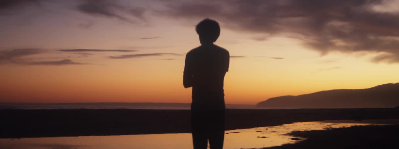 Silhouette of a man standing on an empty beach during sunset