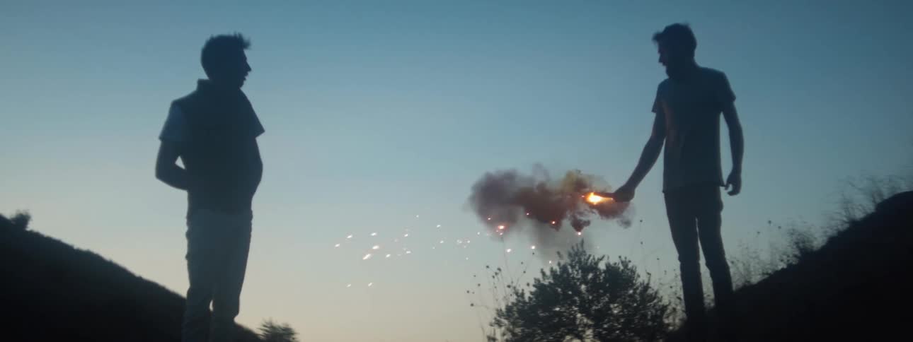 Silhouette of a group of friends burning fireworks on a hill at evening