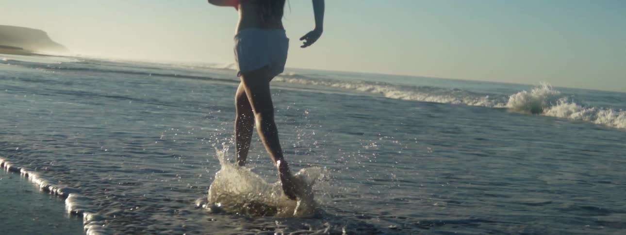 Close up of a barefoot man running on the shallow water on the coast of the ocean at sunset
