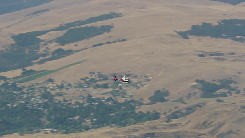 A Medivac Life Flight Rescue helicopter flies over a hilly countryside during the day
