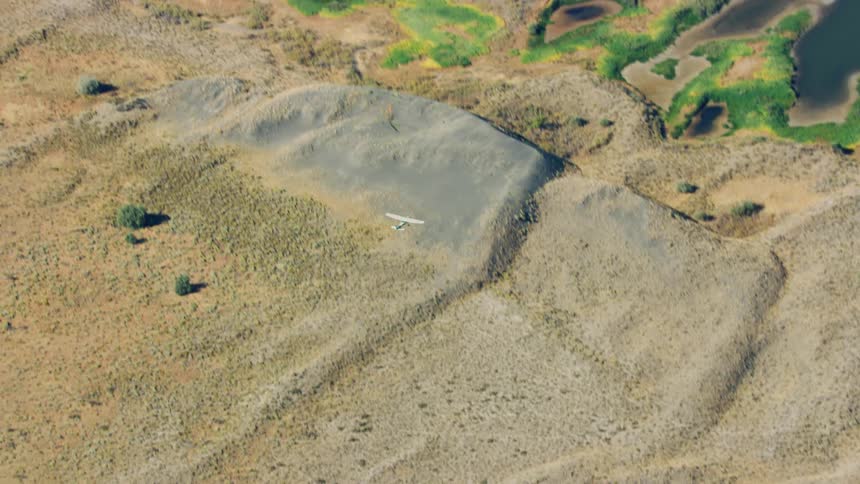 Air to air shot of a small single engine airplane flying over a desert close to scattered lakes surrounded by green algae