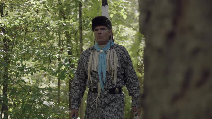A man wearing a fur hat walks in a forest