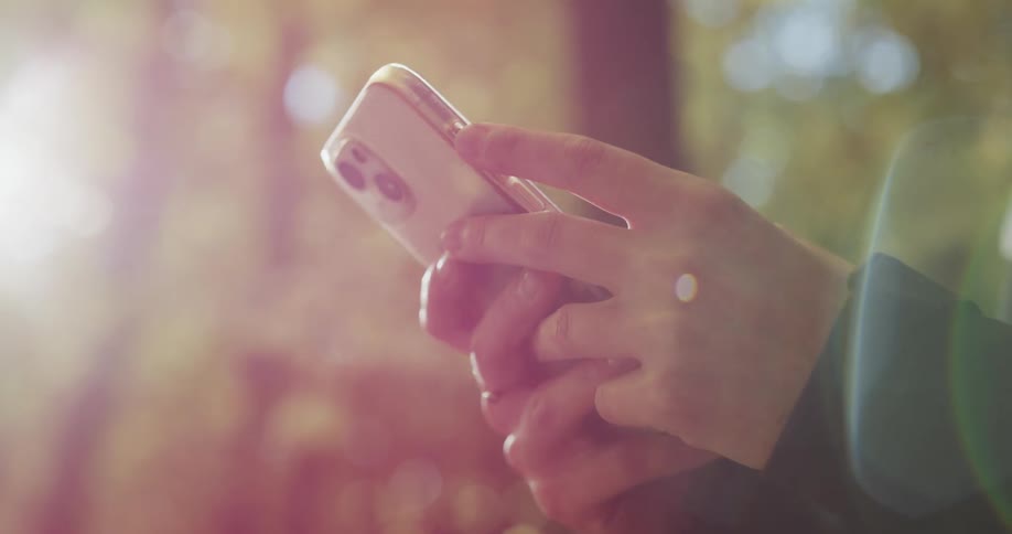 Close up of the smartphone on the hands of a teenager texting in the forest at morning