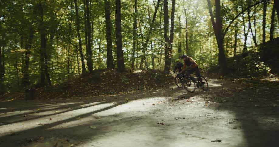 Two people bike down a path in a forest