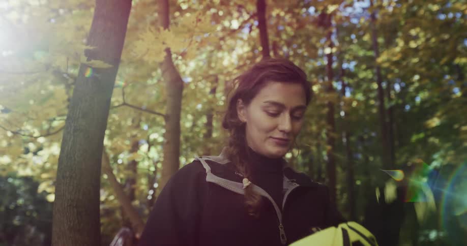 The sun shines brightly through the trees as a woman standing in the woods takes off her cycling helmet and pushes back her hair with her hands