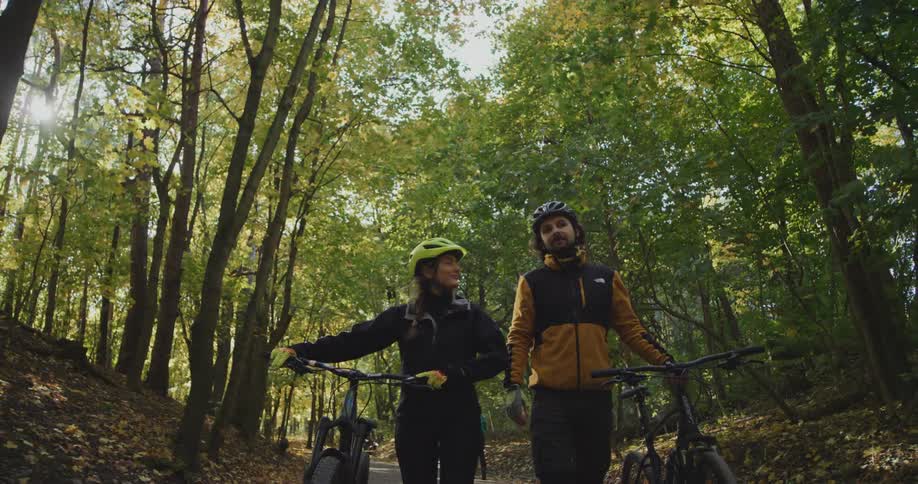 Two older adults are walking on a trail outside with there bike next to them