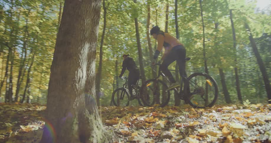 A man and woman cycle through a forest covered in fall leaves