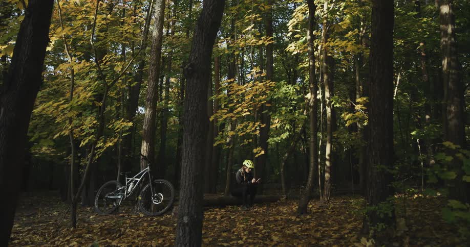A woman props her bicycle against a tree while taking a break to sit on a fallen tree