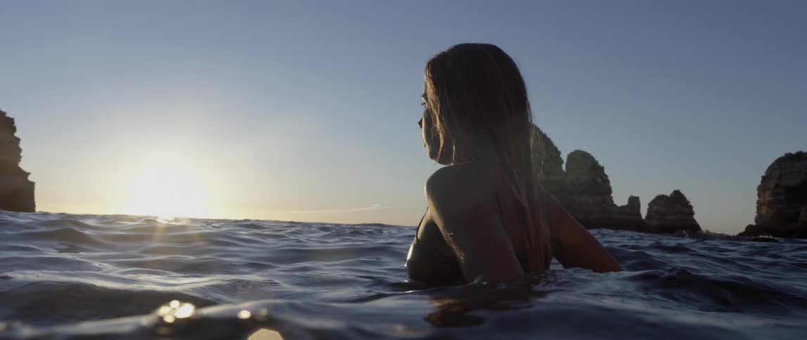A woman stands in the water near a rock formation