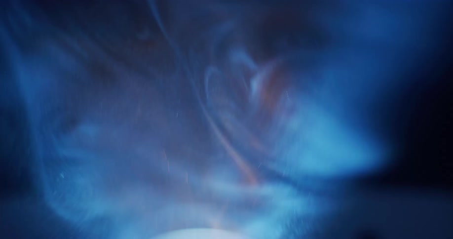 Close up of dust particles floating in front of a bright blue light on a dimly lit room