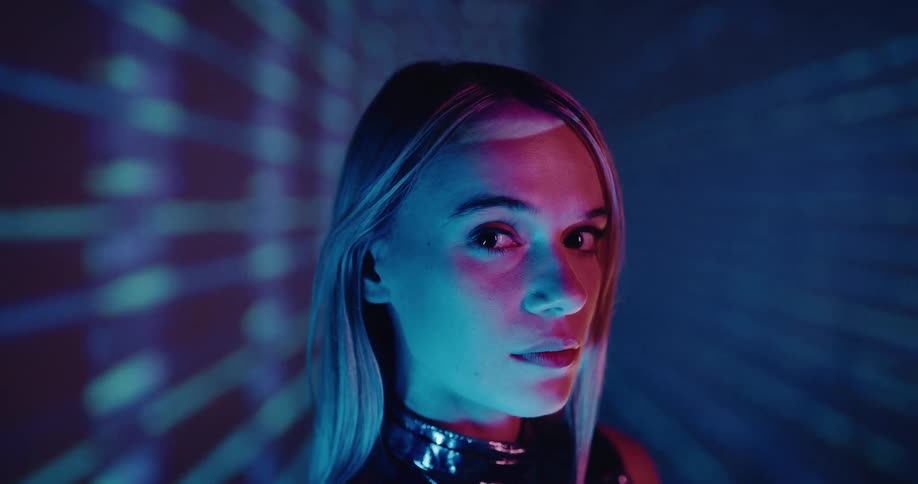A woman with long blond hair is standing in a room with moving lights behind her