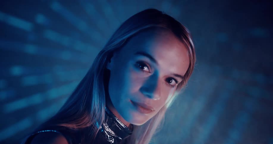 Woman wearing metallic futuristic clothes stands as light show creates zooming effect behind