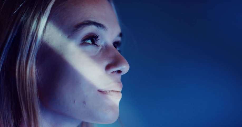 Close up of the face of a young beautiful woman standing on a room under projected blue lights