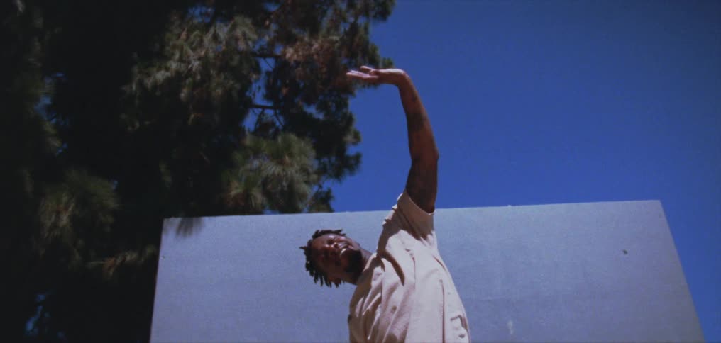 A man holds his hand and twist his body while performing dance moves outdoors