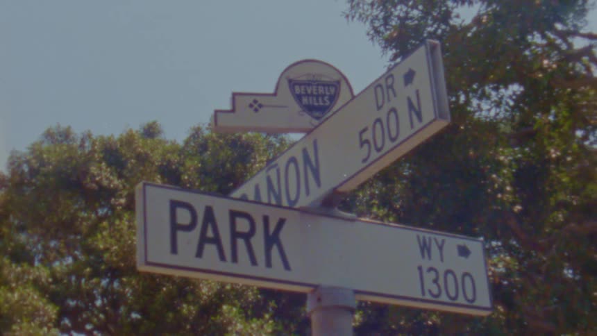 The street sign of two intersecting roads in beverly hills is seen on a sunny day