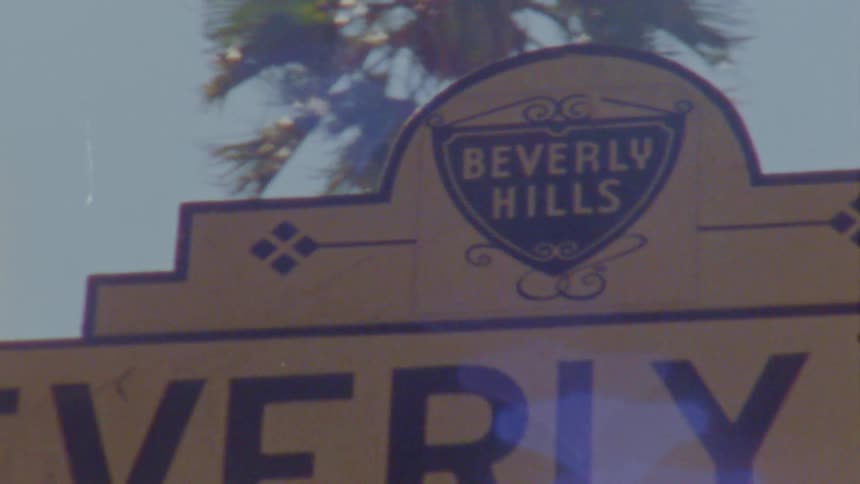 The sun shines upon a sign outside of beverly hills under a clear blue sky
