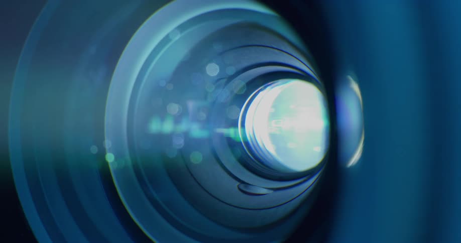 A camera lens in the darkness is emitting moving particles of blue light