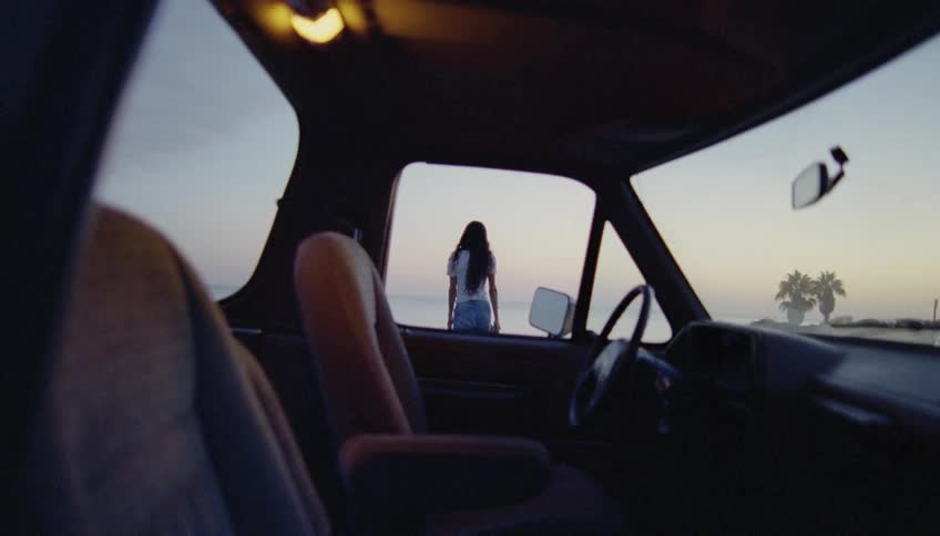 Young woman gets out of a parked car to look at the horizon on the beach at evening