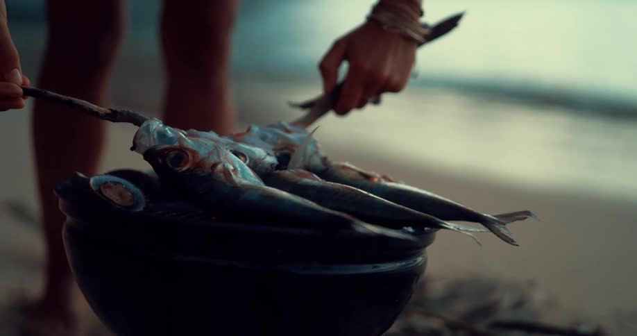 A woman rests three fish across an open fire grill