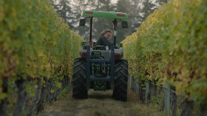 A man is riding on a tractor through farmland