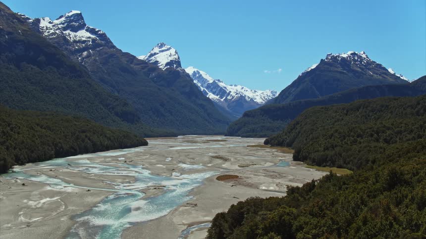 An aerial view of a river running past a forest by a snow capped mountain range