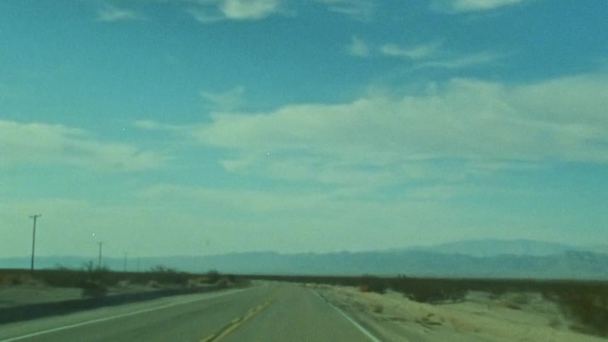 Traveling on a rural highway with mountains in the distance under a blue cloudy sky