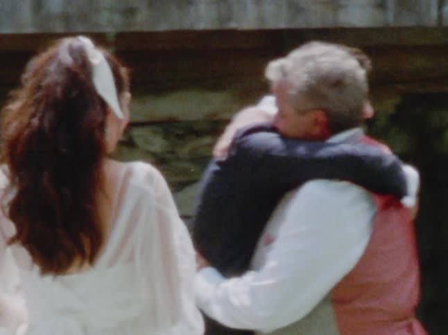 The groom hugs the father of the bride at an outdoor wedding