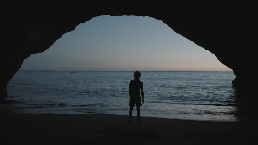Man standing on a beach with rocky overhead
