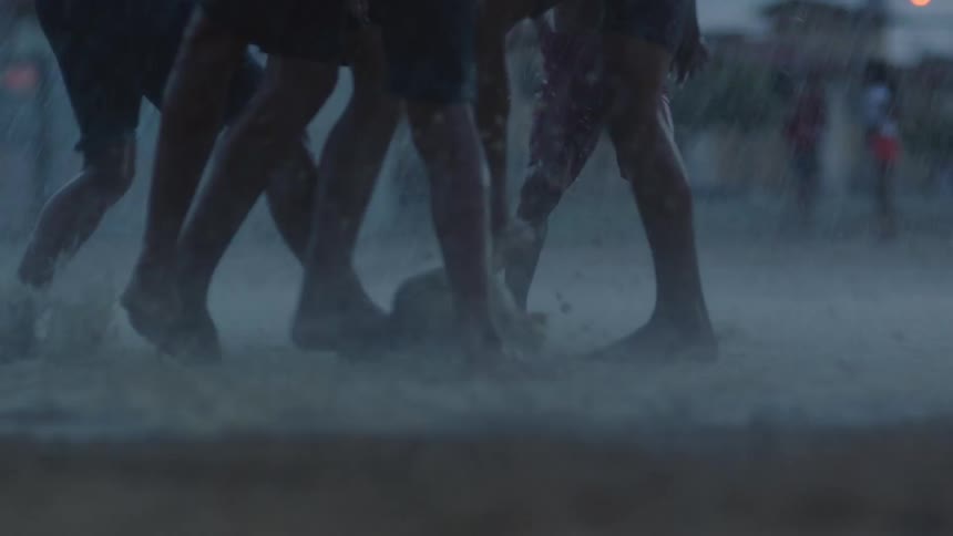 A group of boys are splashing in the water and mud as they play soccer in the rain