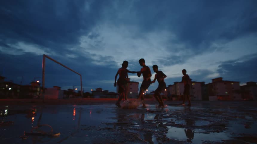 A group of boys run and jump in puddles near apartment buildings