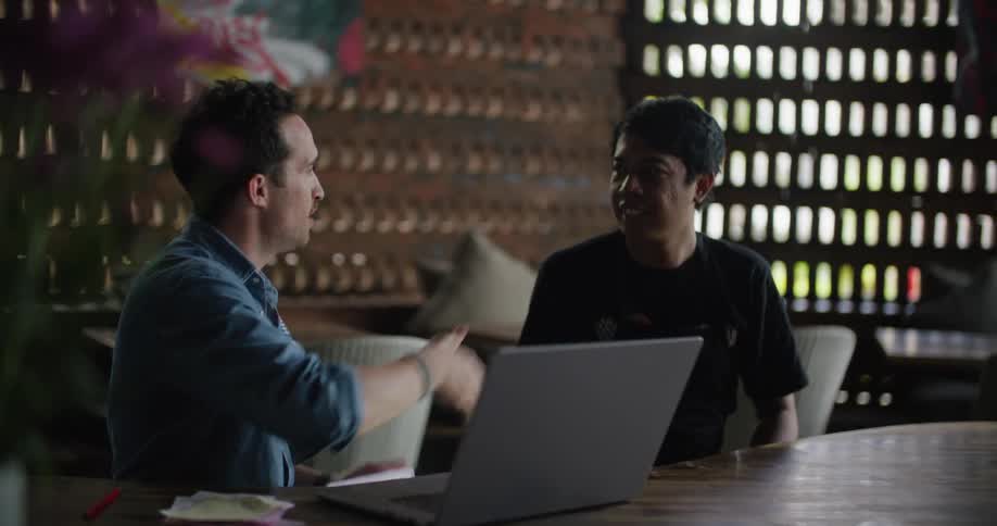 Two men shaking hands over a laptop while sitting at a table