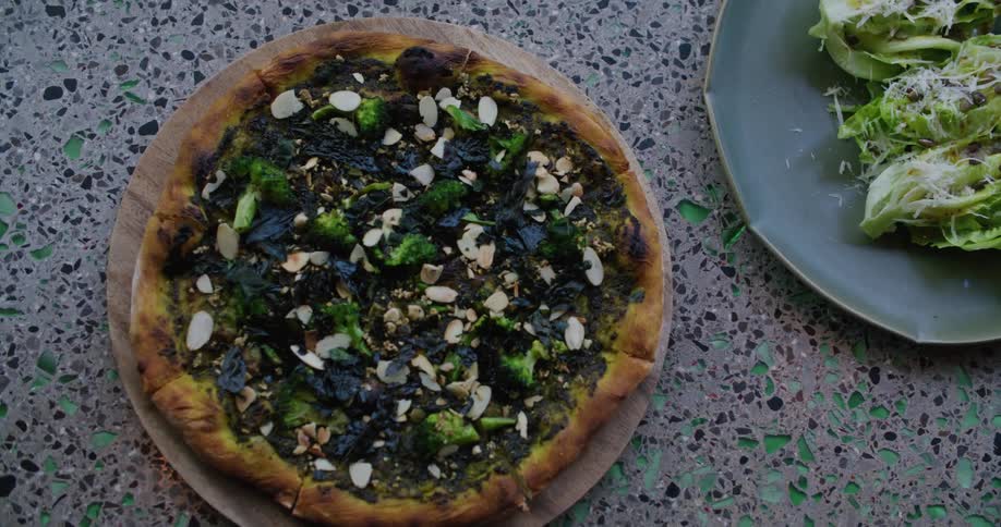 A man sets a pizza down on a table next to salad