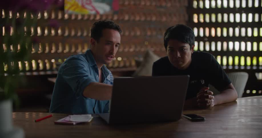 Two men sit in an office while one shows the other something on a computer
