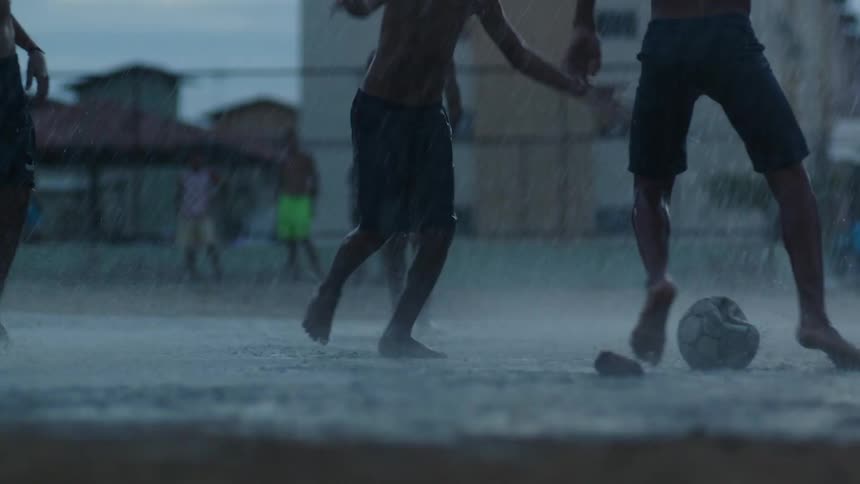A group of boys are splashing in the water and mud as they play soccer in the rain