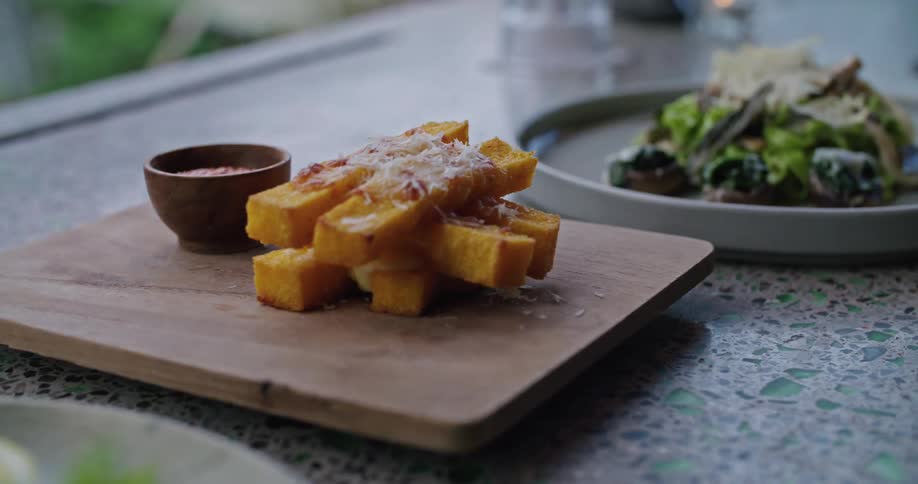 On a table is a cutting board with some appetizer on it located next to a plate of salad