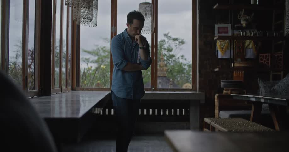 Man paces back and forth near table lining windows while thinking