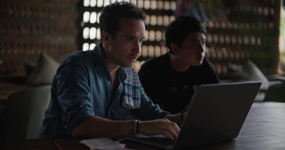 Two restaurant workers check paperwork while working on a laptop