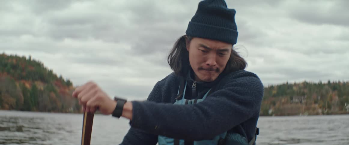 A man in warm clothes paddles his canoe through a large body of water