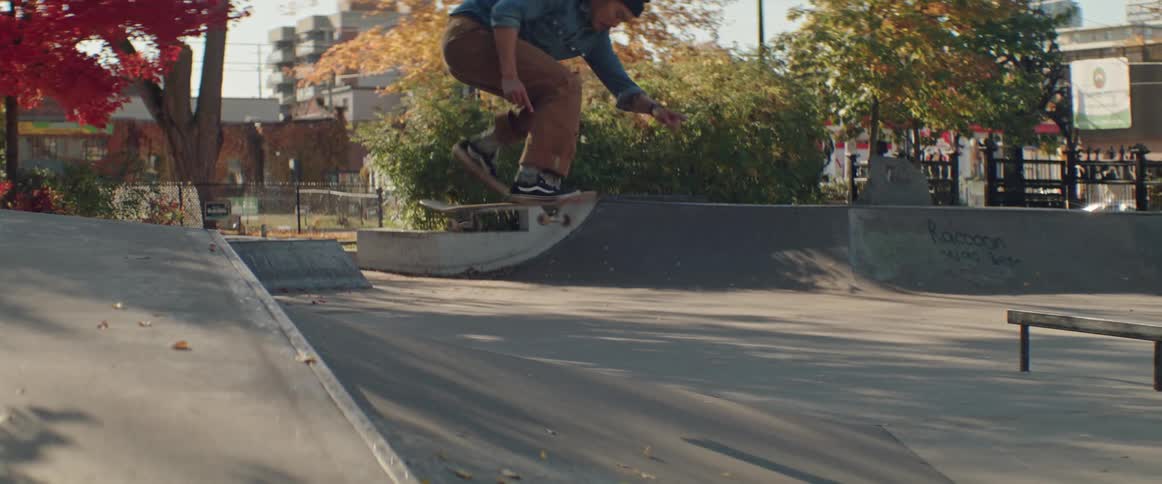 Male skateboarder performs trick on ramp in skatepark as traffic passes on nearby street